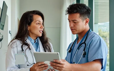 Ärztin mit Stethoskop bespricht mit einem Kollegen auf dem Tablet den nächsten Patienten