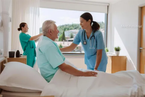 Pflegefachfrau hilft einem älteren Patienten im Spitalzimmer beim Aufsitzen
